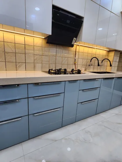 A close-up of the hob and sink area, highlighting the sleek handles and high-gloss finish of the cabinets.