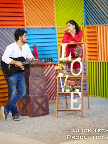 A playful and colorful shot with the groom playing a guitar while the bride poses on a 'LOVE' themed shelf.