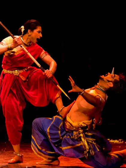 A dramatic scene from a production, likely depicting the story of Durga and Mahishasur. The powerful pose of the female dancer over the male dancer captures the essence of Shakti.