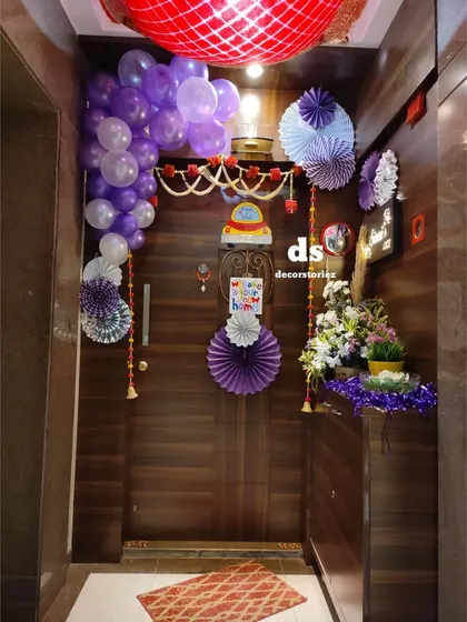 We decorated this home entrance to welcome a new baby. The decor includes a balloon garland, paper fans, a traditional toran, and floral arrangements, creating a warm and festive entryway for guests.