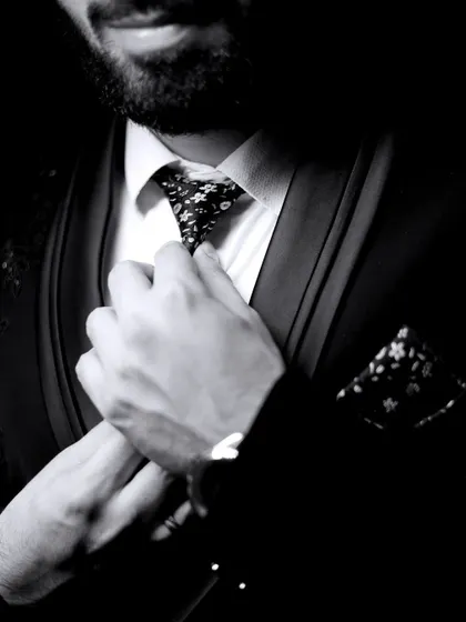 A detailed, artistic black and white shot of the groom adjusting his tie. This focuses on the small details that complete the look.