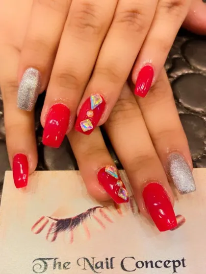 A bright and bold set of red square nails. The look is elevated with silver glitter accent nails and geometric iridescent stones on the middle fingers.
