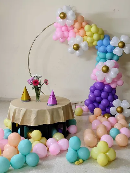 A whimsical and simple birthday setup with a pastel balloon garland featuring balloon daisies. A small table is set for an intimate celebration.