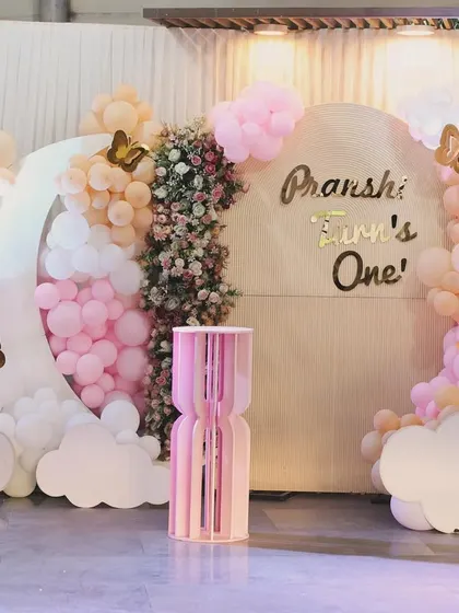 A dreamy and whimsical first birthday for Pranshi. The decor features a moon-shaped balloon frame, fluffy clouds, and gold butterfly accents in a lovely pink and peach palette.