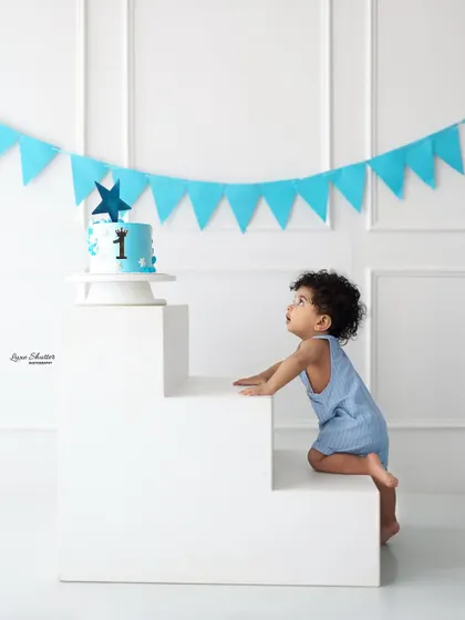 A candid shot of the birthday boy looking up towards his cake, ready for the fun to begin. The simple setup with a blue banner is perfect for this classic theme.