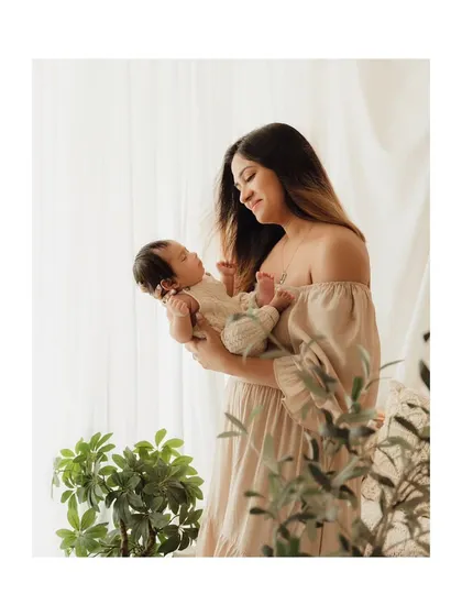 A full-length portrait of a mother holding her baby, captured with beautiful, soft window light.