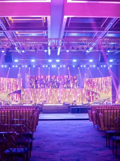 A wide view of a luxurious Sangeet, where dramatic stage lighting in hues of purple and gold transforms the ballroom into an opulent concert-like venue.