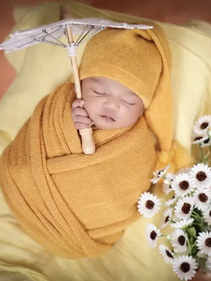 Adding a touch of whimsy with a tiny umbrella prop. This close-up on the sleeping newborn in a yellow wrap highlights the creative and gentle approach we take in our baby photoshoots.