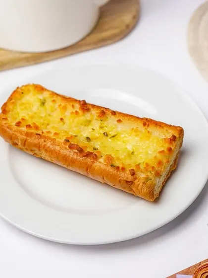 A single piece of cheesy garlic bread on a white plate, with a golden fork nearby. The simple, clean presentation makes this popular appetizer look delicious and ready to eat.