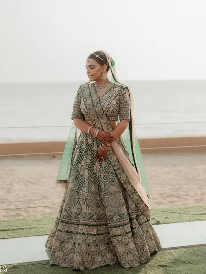 A serene portrait of the bride standing by the beach, her green lehenga contrasting beautifully with the sand and sea.