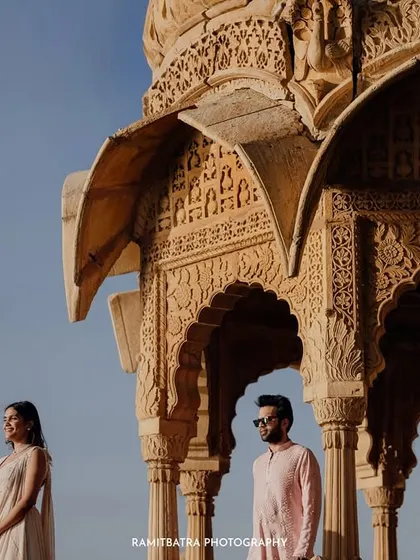 A stylish portrait of the couple standing apart yet connected, framed by the intricate architecture of a Jaisalmer cenotaph.