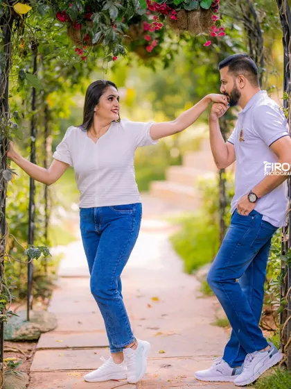 A chivalrous hand-kiss in a beautiful garden archway. This classic romantic gesture, combined with casual modern outfits, creates a timeless yet fresh look.