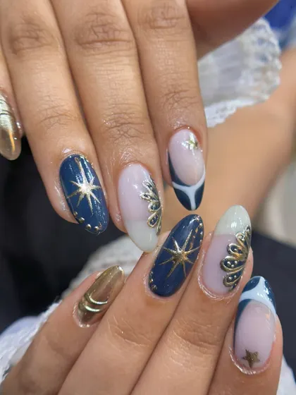 A side view showcasing the 3D elements and metallic shine of this custom nail art set. The raised gold details catch the light beautifully against the deep blue and soft white base colors.
