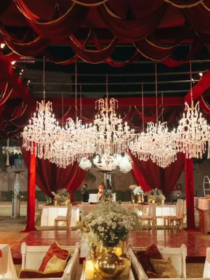 A magnificent wedding setup featuring a canopy of rich maroon drapery and a collection of crystal chandeliers, creating a luxurious and opulent atmosphere for a royal-themed wedding dinner.