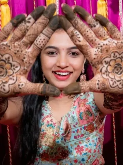 A happy bride framing her face with her beautifully decorated hands. The symmetrical mandala design is a classic choice for bridal mehendi.