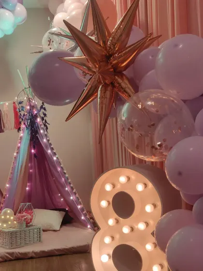 Creating a magical atmosphere is key for a slumber party. A large light-up number '8' and a metallic starburst balloon add a touch of sparkle and fun to the teepee and balloon arrangement.