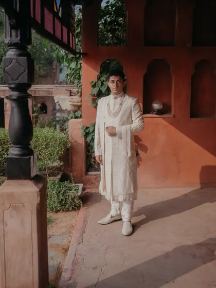 A solo portrait of the groom in his white sherwani, looking regal and composed against the warm, textured walls of Neemrana fort.