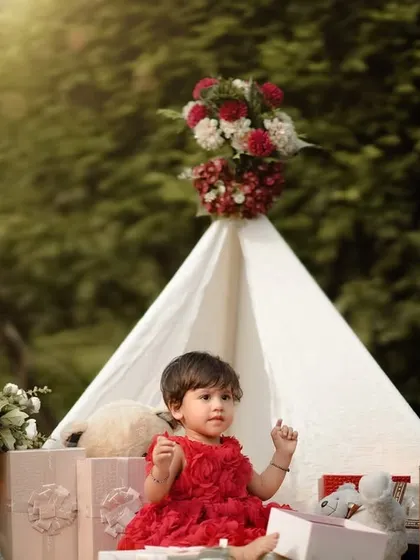 A little princess in her garden castle. This beautiful teepee setup, adorned with flowers and surrounded by presents, is perfect for a first birthday celebration.