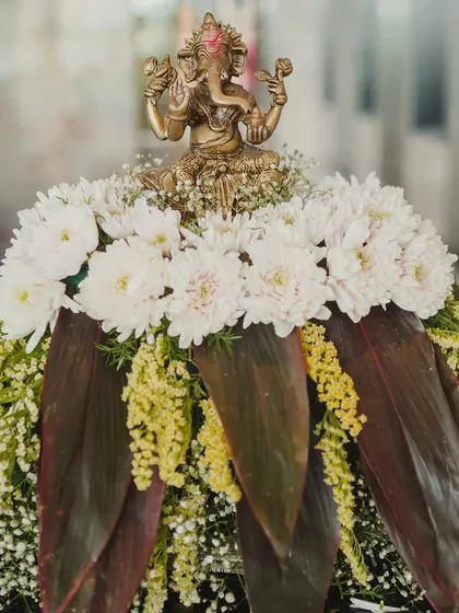 A Ganesh idol placed on a beautiful arrangement of white chrysanthemums and dark leaves, a tradition we follow to bring auspicious beginnings to every event.