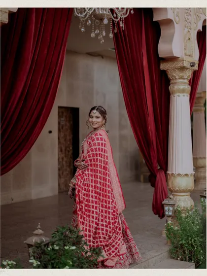 The bride looks back over her shoulder, framed by dramatic red curtains.