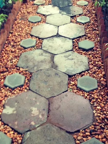 A creative pathway design using different sizes of hexagonal stones set in a bed of pebbles, bordered by plants and a brick edge.