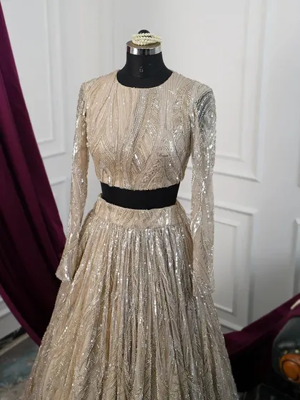 A close-up of the gold sequin lehenga top, showing the texture and pattern of the embellishments. The long sleeves and round neck offer a chic and sophisticated silhouette.