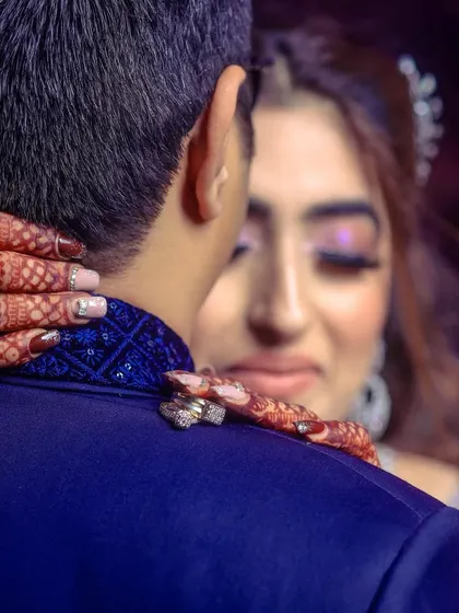 A close-up shot focusing on the bride's hands on the groom's shoulders, showcasing her henna and rings.