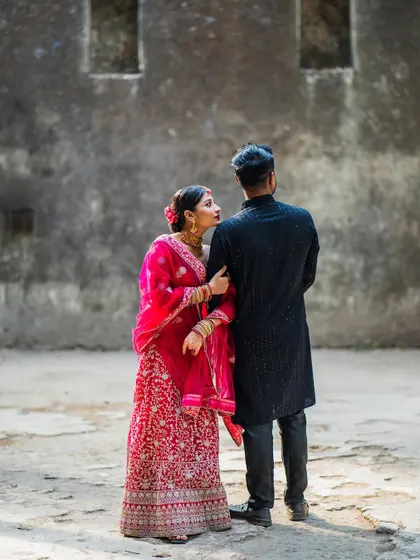 A candid pre-wedding shot from behind the groom-to-be, capturing the bride-to-be's loving gaze as she holds his arm.