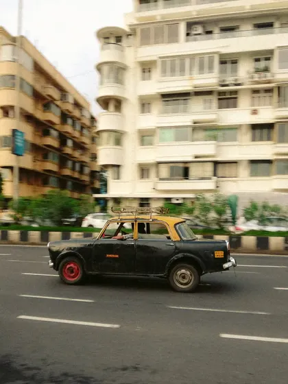 A panning shot of a Kaali-Peeli taxi in motion along Marine Drive. The motion blur in the background conveys speed and energy, capturing the taxi as a dynamic part of the city's landscape.