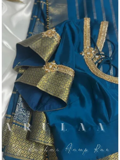 A teal blue blouse where we've used the saree's heavy zari border to create statement bell sleeves. A small embroidered brooch adds a finishing touch.