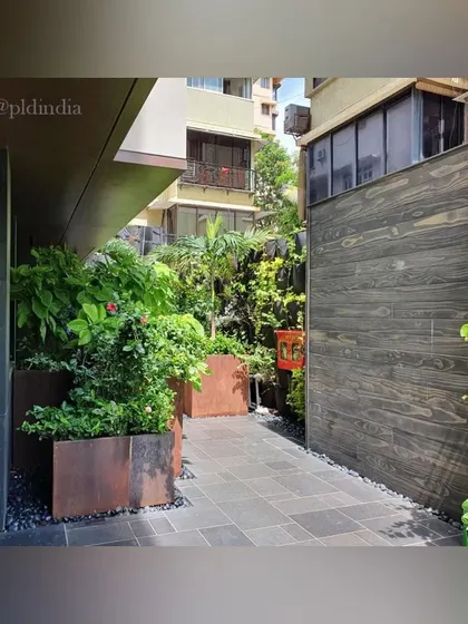 This walkway combines modern materials like dark wood paneling and Corten steel planters with lush, flowering plants, creating a sophisticated and welcoming entrance path.