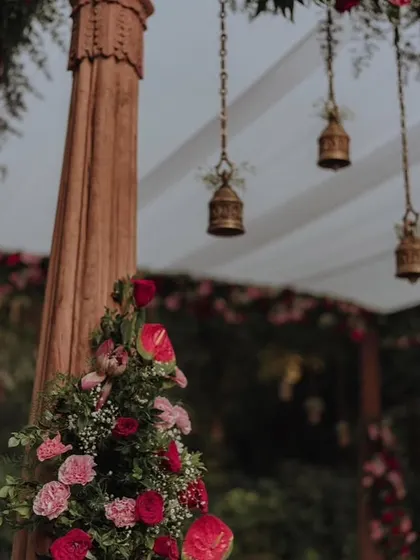 A close-up of our mandap decor, showing the detail of carved wooden pillars, hanging temple bells, and fresh floral arrangements.