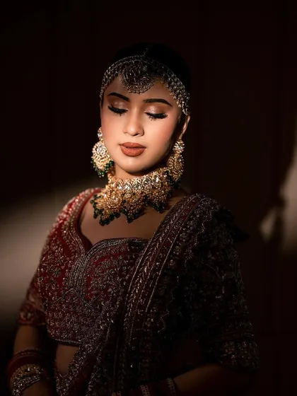 An artistic shot capturing the bride in a moment of reflection. The dramatic lighting highlights the flawless finish of her makeup, from the smooth base to the expertly applied eye details.