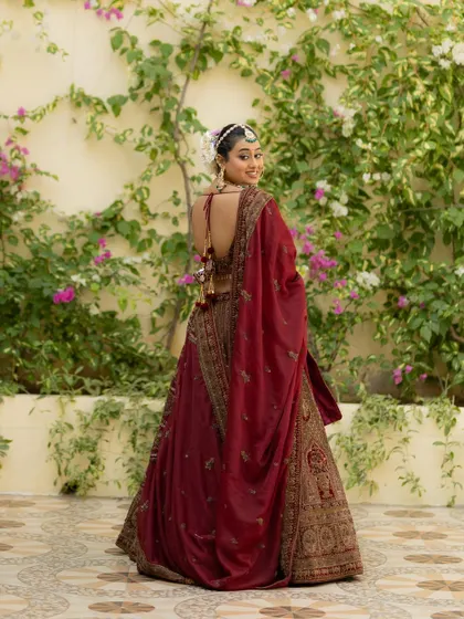 The bride looks back over her shoulder with a smile, showing off the beautiful back design of her blouse against a floral wall.