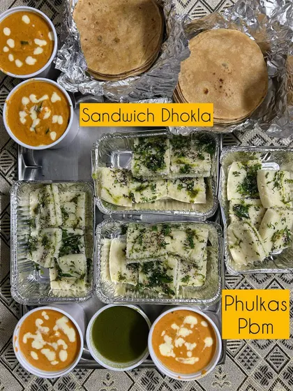 A meal featuring my Sandwich Dhokla, which has a layer of green chutney in the middle, served with Paneer Butter Masala and Phulkas.