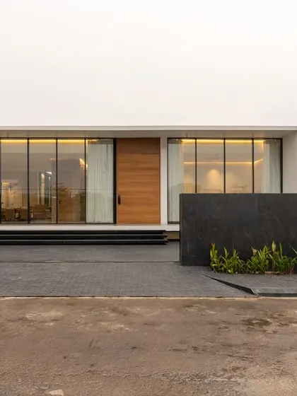 The entrance to the courtyard house is marked by a clean, minimalist facade and low, dark stone walls that guide the visitor. The design is deliberately understated, hinting at the light-filled, nature-connected spaces that lie within.