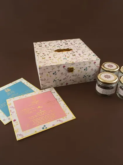 A charming floral-printed box with a rustic feel. This invitation set includes colorful inserts and four small jars, making it a delightful and generous announcement.