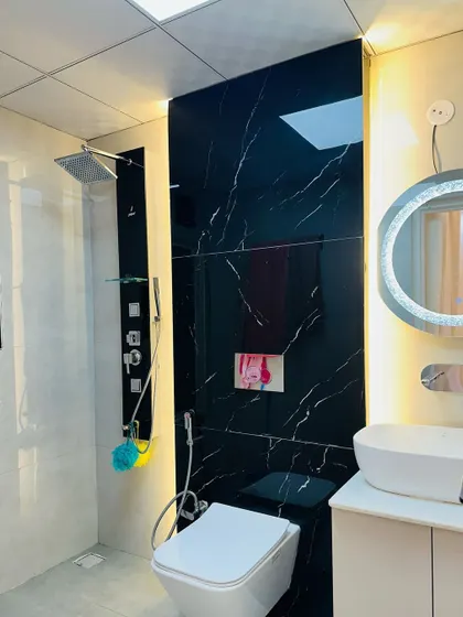 A close-up of a bathroom with a black marble-finish shower panel. The design includes a modern shower system and a circular backlit mirror, creating a bold and contemporary look.