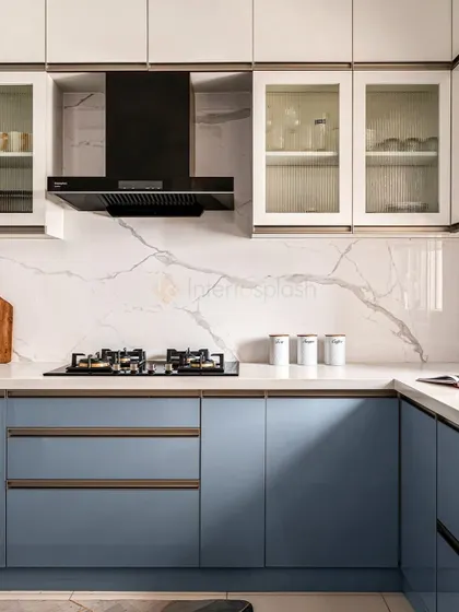 A closer look at the cooking area in the blue and white kitchen. The design features a sleek black chimney, an induction cooktop, and a mix of drawers and glass-front cabinets for varied storage.