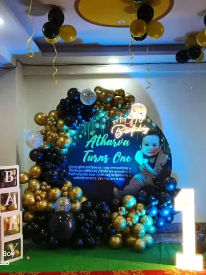 A stylish first birthday setup with a 'Boss Baby' theme. The decoration features a personalized circular backdrop, a black and gold balloon arch, character cutouts, and a light-up marquee number '1'.
