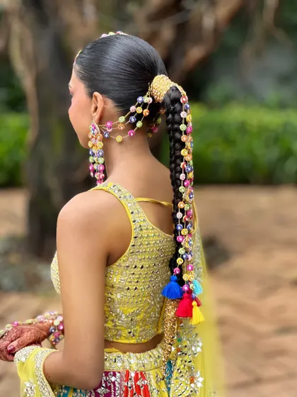 A detailed look at the back of Aish's vibrant Haldi hairstyle. This long, thick braid is intricately woven with colorful beaded accessories and tassels for a truly unique and festive look.