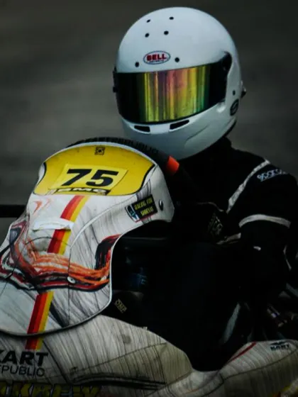 A driver sitting on his kart, holding his helmet.