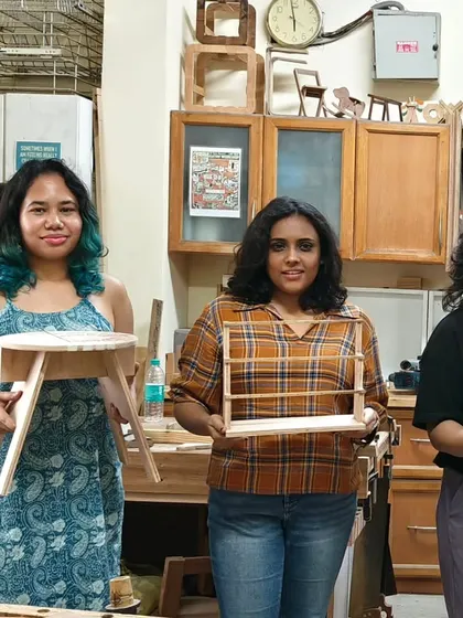 Three participants from a Saturday workshop showing off their creations: a small stool, a spice rack, and a decorative wooden tray.
