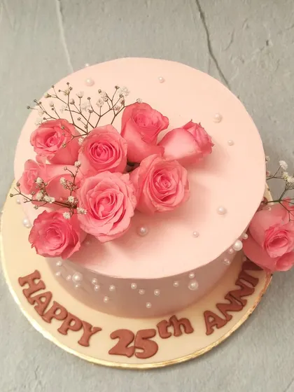 We commemorate a 25th anniversary with timeless elegance. This soft pink cake is adorned with a bouquet of fresh pink roses, sprigs of baby's breath, and scattered pearls, creating a romantic and classic design to celebrate a silver jubilee.