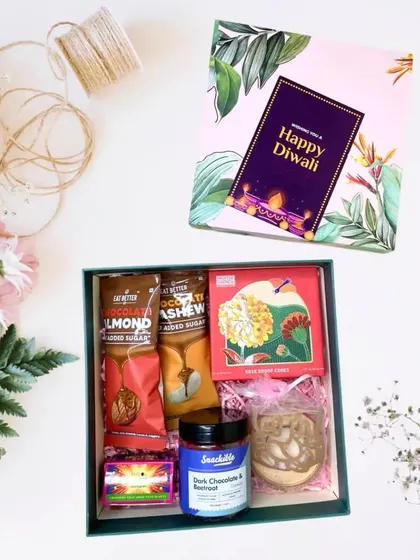 A sweet and thoughtful Diwali hamper. It contains chocolate almond snacks, dark chocolate cookies, and a decorative Ganesha diya, all elegantly packaged.
