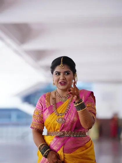 A candid moment of the bride in a vibrant yellow and pink saree. The custom blouse has delicate embroidery on the sleeves that complements the saree's border.