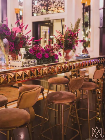 A long shot of the sangeet bar, showcasing the studded gold finish and the line of vibrant floral arrangements that adorn it.