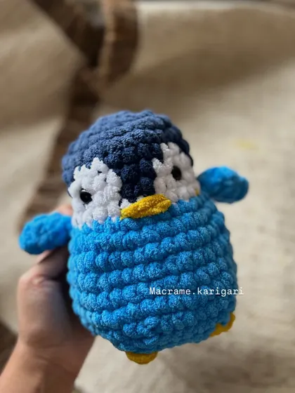 Holding one of our blue chunky yarn penguins. The texture of this yarn is incredibly soft and plush, making it one of our favorite materials for toys that are meant to be cuddled.