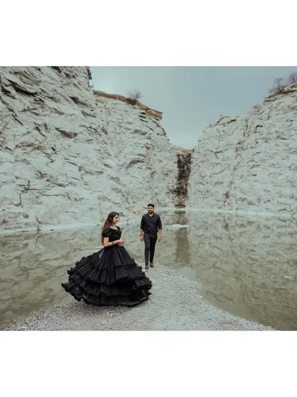 A bride in a flowing black gown stands on a spit of land in a quarry lake, with her groom behind her. A dramatic and artistic composition.
