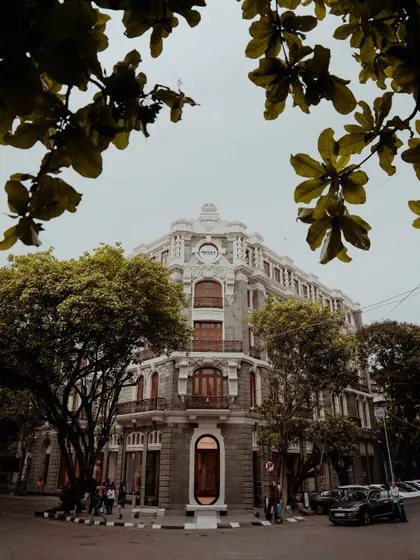 A series of photographs capturing the architectural memory of old Bombay. These images feature landmarks like the Rajabai Clock Tower, the Asiatic Society Library, and other colonial-era structures, often framed by trees.
